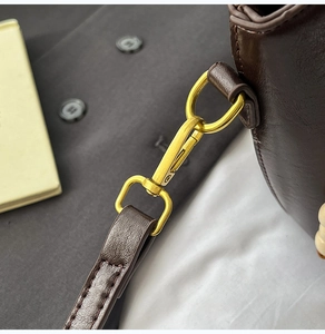 Detail of matte gold metal hook on soft dark brown leather bucket bag with fine stitching