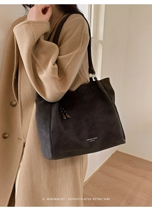 Detail of dark charcoal leather tote bag with plush charm and branding on long tan coat
