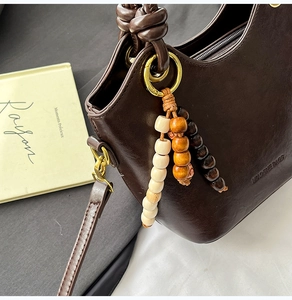 Detail of dark brown leather bucket bag with tricolor wooden bead charm and knot handle