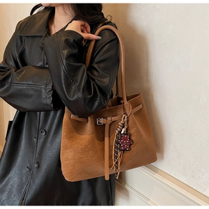 Detail of vintage brown tote bag with bear charm and tassel on black leather jacket