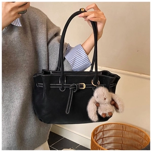 Detail of black leather tote bag featuring white contrast stitching and a plush rabbit charm
