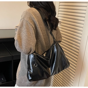 Detail of a large black glossy tote bag with silver ring accents on a shoulder strap