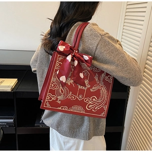 Detail view of red bridal handbag with gold embroidery and silk bow on shoulder