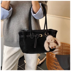Detail of black tote bag with white stitching and cute plush rabbit charm accessory