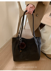 Detail of soft charcoal tote bag with plush charm on minimalist wooden floor
