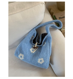 Detail of blue plush tote bag featuring white floral embroidery and dark toggle closure