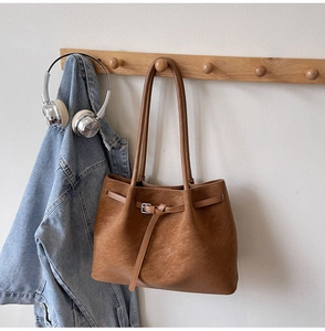 Close-up of brown PU leather tote bag with decorative strap and fine texture hanging on a rack