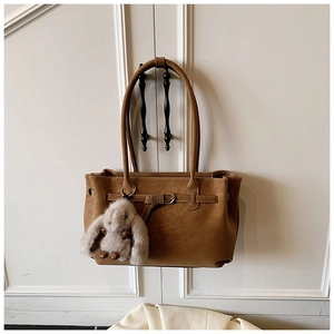 Detail of a brown leather tote bag with a decorative buckle and a white plush bunny charm