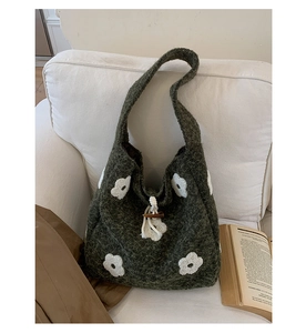 Detail of green knitted tote bag featuring floral embroidery and wooden button closure
