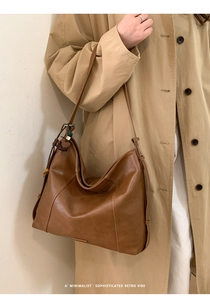 Modèle portant un sac hobo en cuir marron foncé avec pompon latéral décoratif