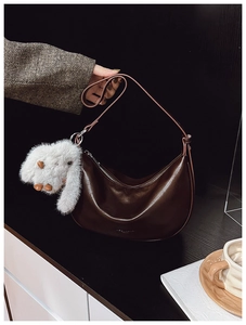 Detail view of a dark brown faux leather hobo bag with a white plush bunny charm