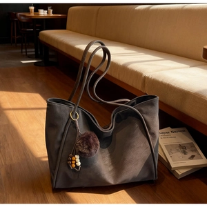 Detailed texture of dark brown faux leather tote bag with decorative bead and pompom charm