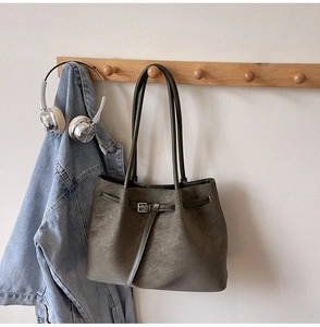 Detail of dark olive green tote bag hanging on wooden rack with casual denim jacket