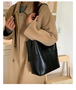 Détail d'un sac seau noir en similicuir grainé sur un manteau en laine de couleur camel