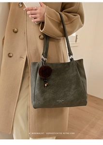 Close-up of a large olive leather tote bag worn with a camel coat and fur pompom