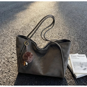 Close-up of charcoal grey leather tote bag with a brown pompom charm on asphalt