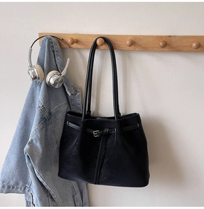Detailed view of black tote bag hanging on a wooden hook with denim jacket and headphones