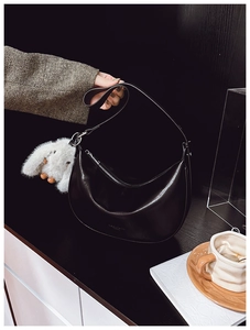 Detail of a black half-moon shoulder bag with a cute white rabbit plush charm and zip closure