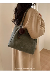 Detail of dark green leather tote bag with brown pom-pom and braided cord charm on strap