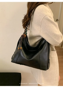 Gros plan d'un sac hobo noir avec breloque fleurie et pompon en perles de bois