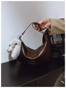 Detail of dark brown crescent bag featuring a grey plush bunny pendant and metal zipper