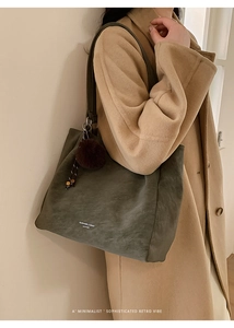 Detail of dark olive suede tote bag with brand logo and soft pom-pom keychain