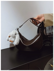 Detail of a brown half-moon hobo bag with a soft white plush bunny charm and textured surface