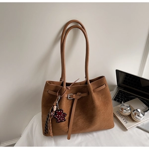 Detail of dark caramel suede tote bag with metal buckle, tassel, and bear charm