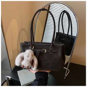 Detail of dark vintage leather tote bag with white stitching and plush rabbit charm
