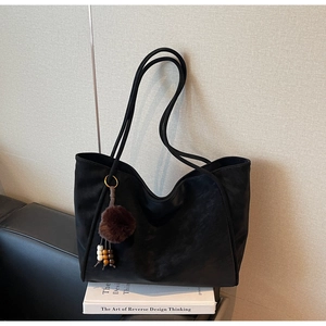 Detail of black matte tote bag featuring a brown fluffy keychain and long shoulder strap
