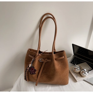 Detail of a brown suede tote bag with bear charm next to a laptop and headphones