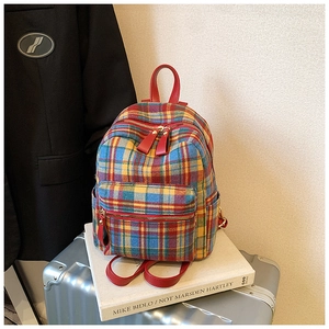 Close-up of vintage plaid backpack showing red leather handles and multi-layer zippers
