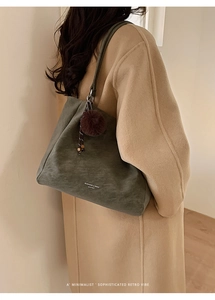 Detail of sage green suede tote bag with fur ball charm and branded text on strap