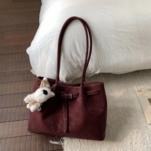 Dettaglio della borsa tote in pelle bordeaux con manico lungo e ciondolo a forma di cucciolo