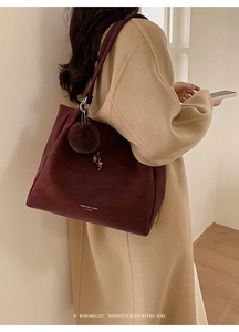 Detail view of large burgundy suede tote bag with logo and plush ball keychain on model