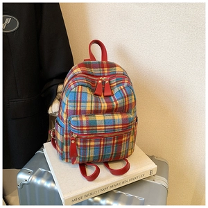Close-up of multicolor plaid backpack fabric with red leather straps and metal zippers