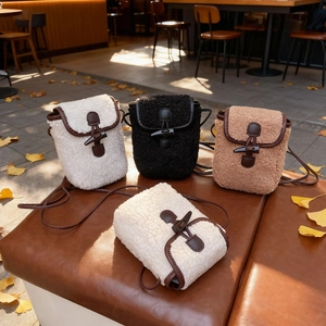 Three colors of faux shearling crossbody bags with horn buckles on an outdoor bench