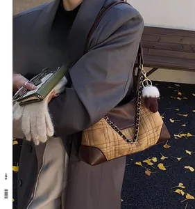 Detail of checkered hobo bag with gold chain strap and plush ball charm in autumn setting