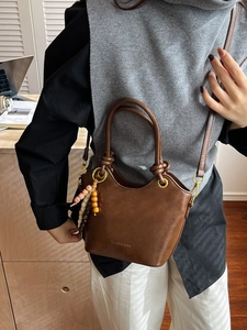Retro dark brown bucket bag with twisted handle and ethnic bead charm on a shoulder strap