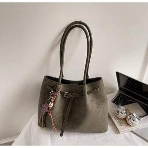 Green leather tote bag with long strap and charm beside laptop and books