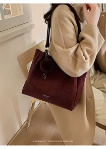 Detail of wine red leather tote bag with brown pompom charm and minimalist brand lettering