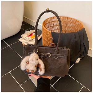Detail of a dark brown suede tote bag featuring a cute rabbit charm and a strap buckle