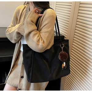 Detail of black tote bag featuring a brown plush ball charm and colorful wooden beads