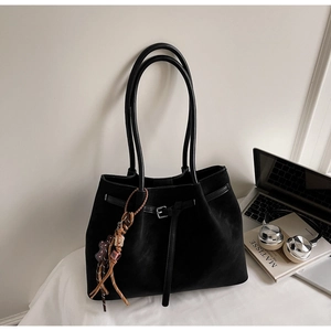 Detail of a black suede tote bag featuring slim handles and woven tassel charm accents