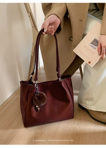 Detail view of burgundy tote bag with plush charm and shoulder straps in retro setting
