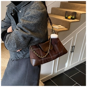 Detail of checkered shoulder bag featuring metal chain strap and plush glove charm
