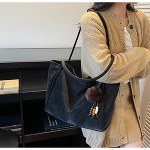 Detail of black faux suede tote bag with decorative plush pom-pom and wooden bead tassel