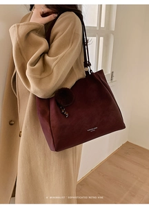 Street style view of a large burgundy tote bag with plush ball charm and logo detail