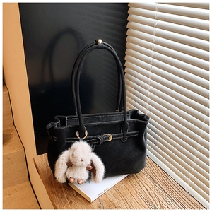 Detail of black tote bag with white stitching, gold buckle, and white bunny charm