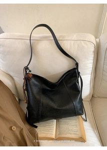 Gros plan du sac cabas noir en cuir ciré vintage avec pendentif fleur sur un canapé